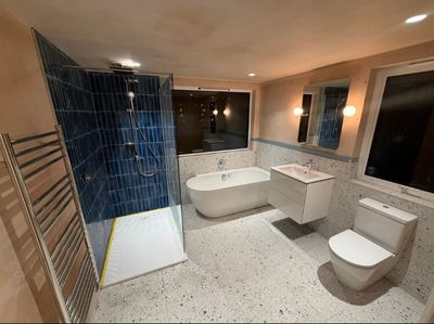 Bathroom with dark blue tiled shower, freestanding bath and terrazzo floor